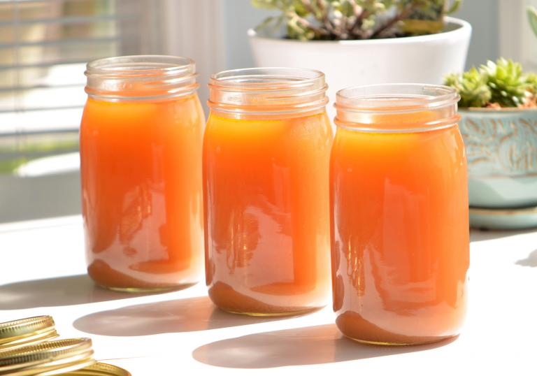 Three mason jars filled with homemade detox broth on a table in the sunlight.